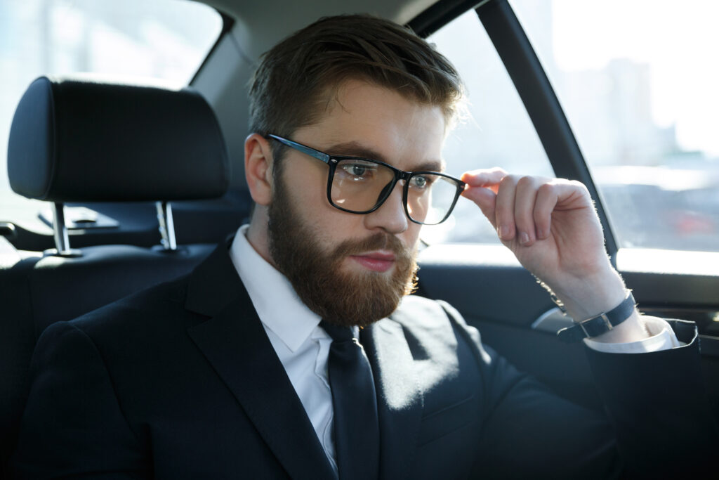 Portrait of a serious young man wearing suit and eyeglasses while sitting in car